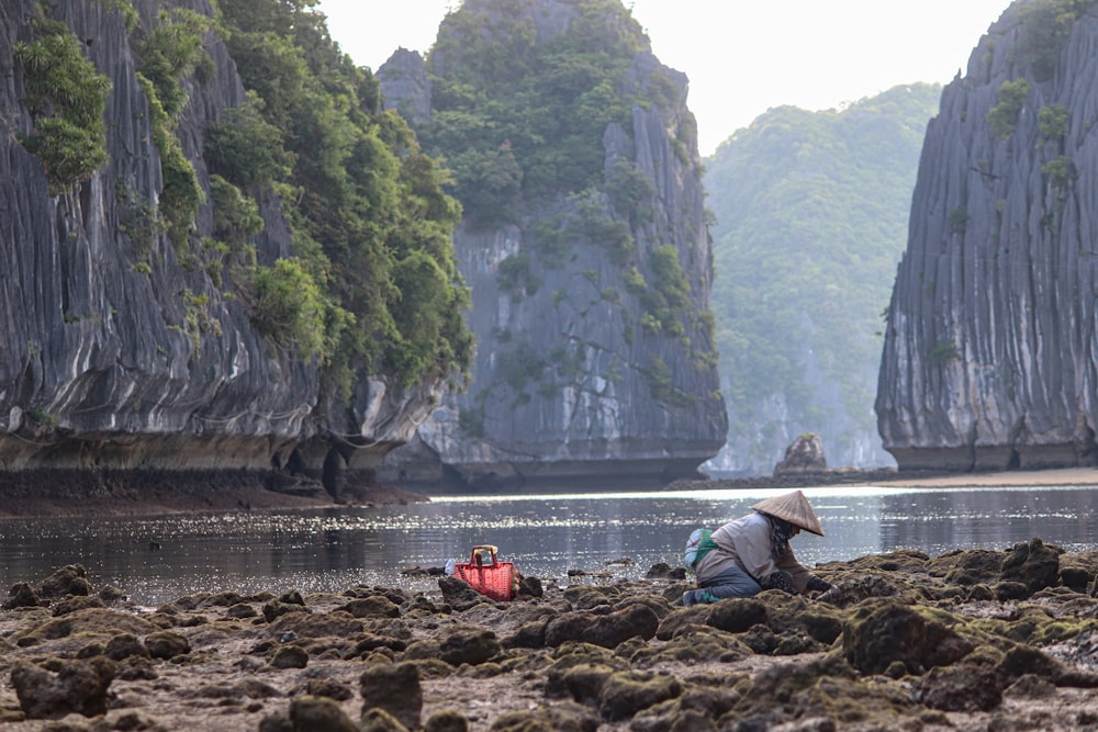 a person sitting on a rocky beach next to a body of water