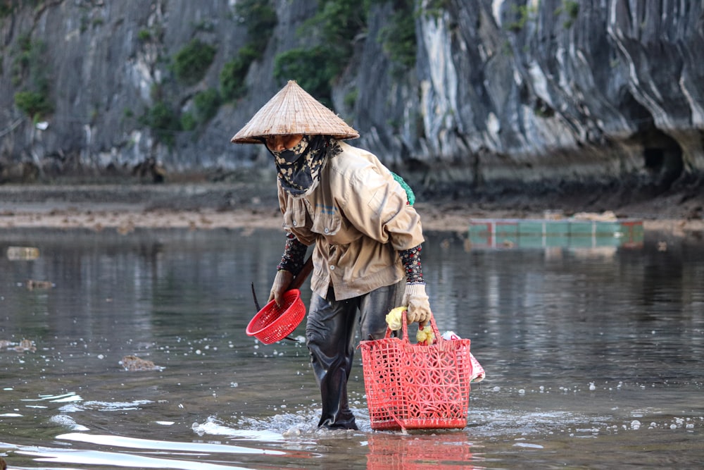 Une femme coiffée d’un chapeau de paille patauge dans l’eau avec un panier rouge