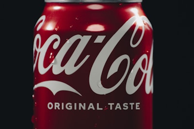 A close-up of a cold soda with condensation beads on the glass, lit by neon red and yellow lights.