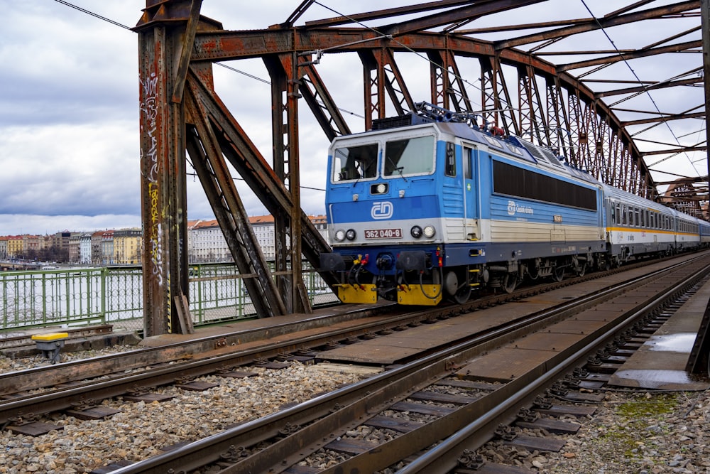 a blue train traveling down train tracks next to a bridge