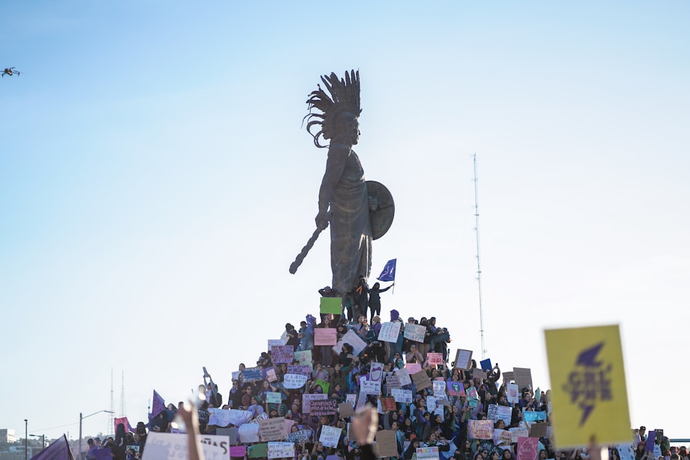 a crowd of people holding signs and standing around a statue
