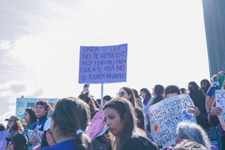 A group of people holding signs during a protest. The signs have messages written in Spanish, and the scene is bright and open. The atmosphere seems active and focused.