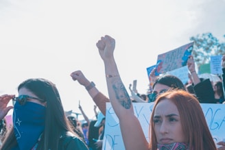A diverse group of Victoria activists raising their elbows and fists in solidarity, with Canadian flags in the background.