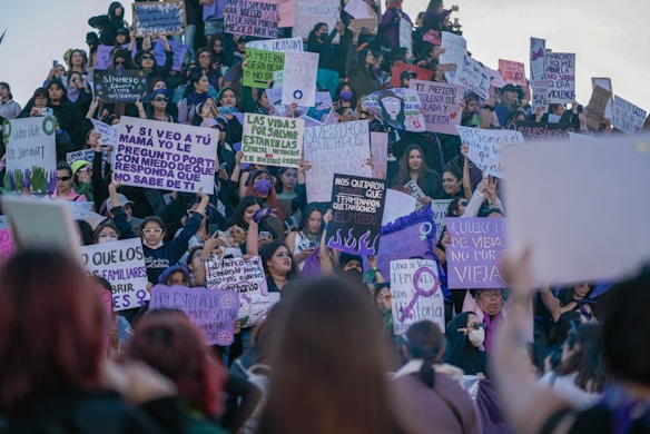 A large group of people, predominantly women, are gathered for a protest or rally. Many are holding signs with messages advocating for rights and against violence. The crowd exhibits a sense of solidarity and determination.