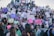 A large group of people, mostly women, are gathered together holding signs with various messages and slogans. The signs are written in Spanish and appear to be advocating for women’s rights or protesting against gender-based violence. The crowd is diverse, with attendees of different ages and expressions, and many have serious or determined looks. The setting appears to be outdoors, possibly on a flight of steps or a sloped surface.