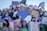 A large group of people gathered in a public demonstration, holding signs with messages related to empowerment and protest. The crowd is diverse, with individuals displaying expressions of determination and solidarity. Many participants are wearing purple clothing or accessories, and one prominently holds a heart-shaped sign.