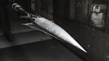 A model of a sleek, pointed aerospace vehicle with a sharp nose and aerodynamic fins is mounted inside a testing environment. The surroundings are metallic and industrial, with a perforated surface and visible instrumentation.