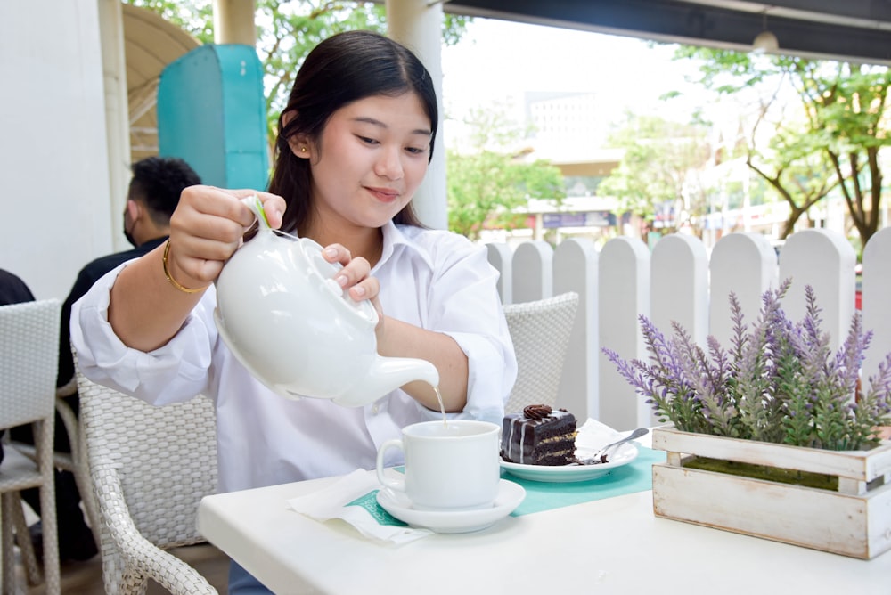 a woman sitting at a table pouring a cup of coffee