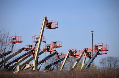 Several cherry picker lifts are extended into the sky, creating a line of machinery against a clear blue backdrop. Each lift features a red and white color scheme with baskets at the top.