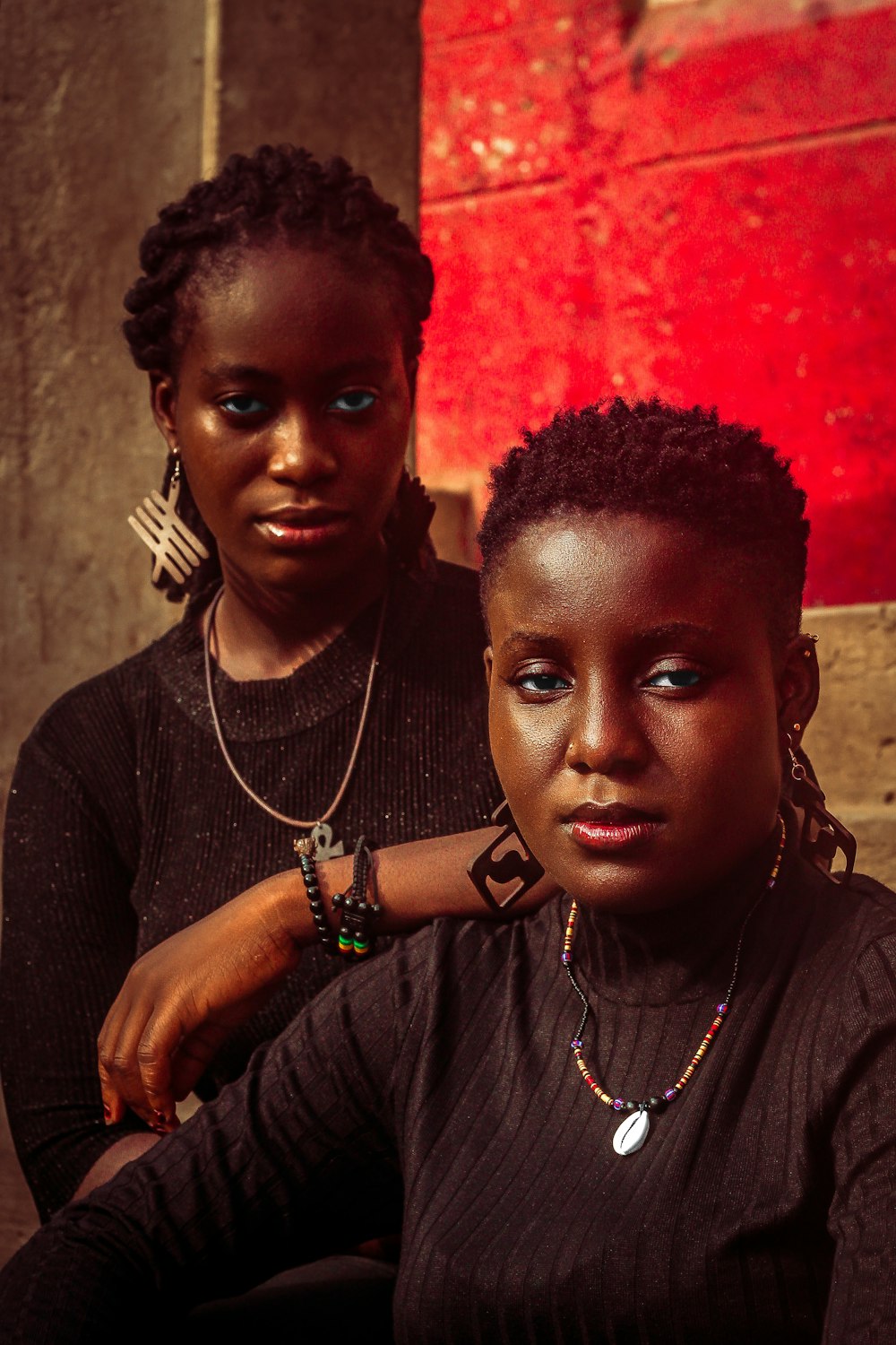 two women sitting next to each other in front of a red wall