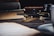 A golden snake-shaped pen lies elegantly on a dark wooden table, surrounded by old books and an ink bottle. The scene is composed with a vintage style, evoking a sense of timelessness and sophistication.