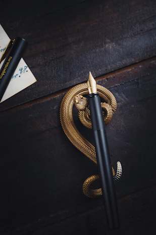 A beautifully crafted brass and resin fountain pen resting on a wooden desk beside an open ink bottle and a neatly wrapped gift box.