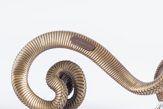 A metallic spiral structure with a ribbed texture, featuring a small embossed label that reads 'COPPER JIS TW'. The object appears rigid and sturdy, with an industrial design aesthetic.