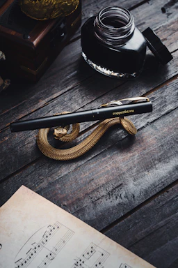 Close-up of a handwritten music score beside a vintage fountain pen on a wooden table.