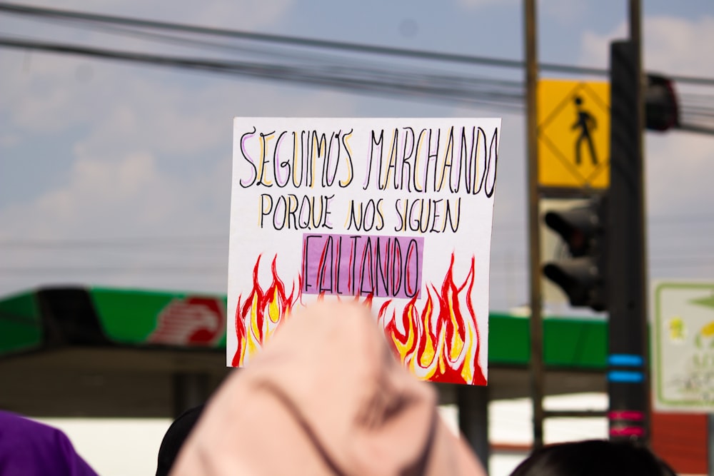 a person holding up a sign in front of a gas station