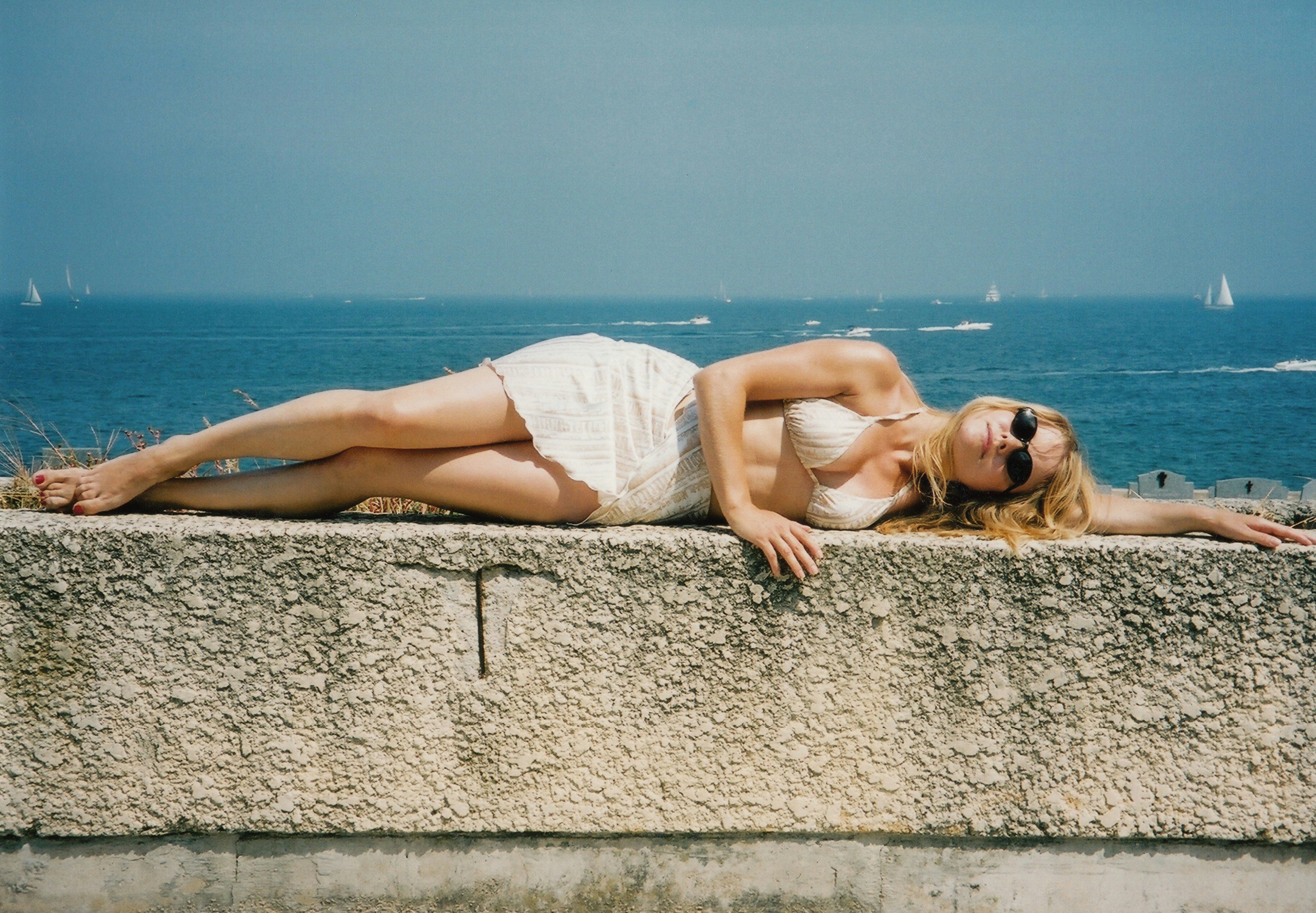 a woman in a white bathing suit laying on a wall next to the ocean