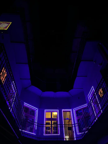A sleek hotel room bathed in soft purple neon light with a view of the city skyline at night.