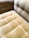 A close-up view of a plush, velvet-tufted cushion on a chair or sofa, showcasing its textured and luxurious finish in a muted golden brown color. The upholstery features a grid-like pattern with deep button tufting.