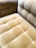 A close-up view of a plush, velvet-tufted cushion on a chair or sofa, showcasing its textured and luxurious finish in a muted golden brown color. The upholstery features a grid-like pattern with deep button tufting.