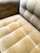 A close-up view of a plush, velvet-tufted cushion on a chair or sofa, showcasing its textured and luxurious finish in a muted golden brown color. The upholstery features a grid-like pattern with deep button tufting.