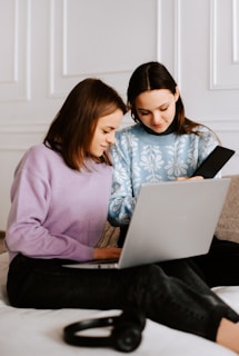 two women sitting on a bed looking at a laptop