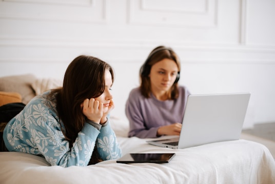 a woman laying on a bed next to another woman on a laptop