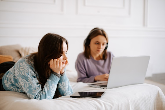 a woman laying on a bed next to another woman on a laptop