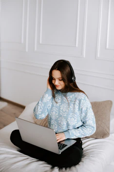 a woman sitting on a bed using a laptop computer