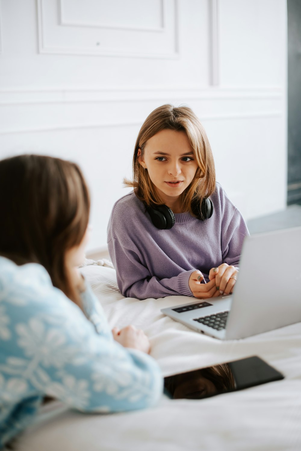 two women sitting on a bed looking at a laptop