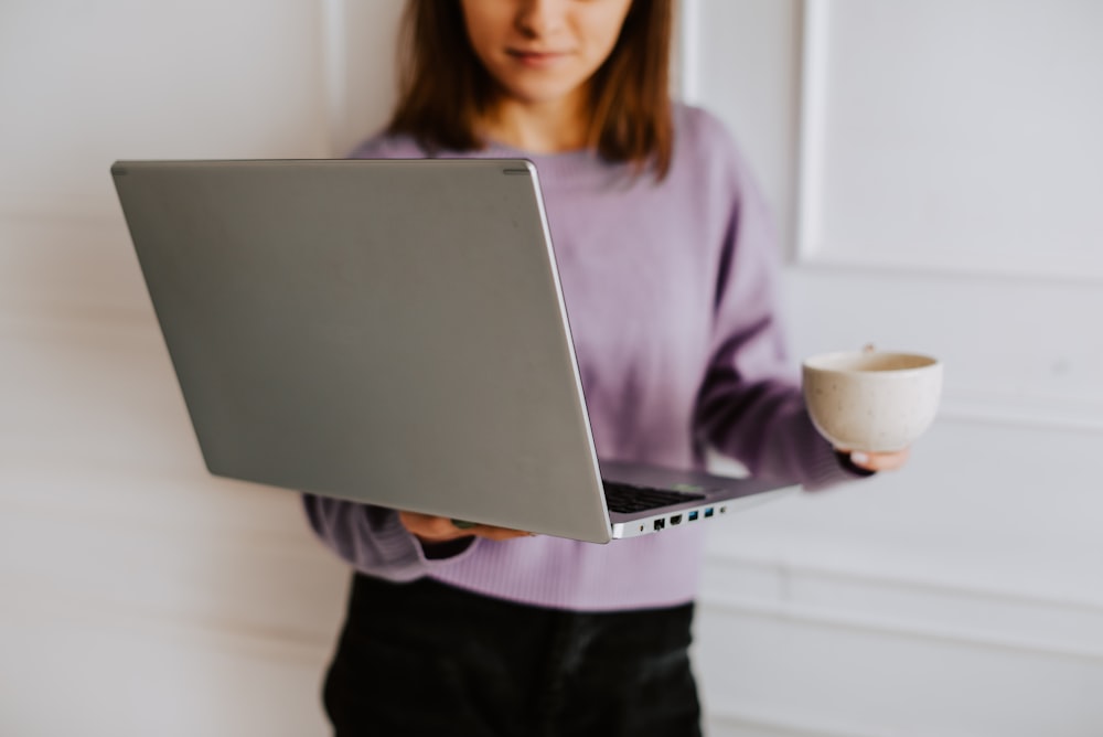 a woman holding a laptop and a cup of coffee