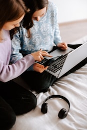 two girls sitting on a bed using a laptop