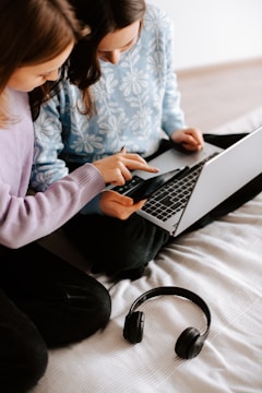 two girls sitting on a bed using a laptop