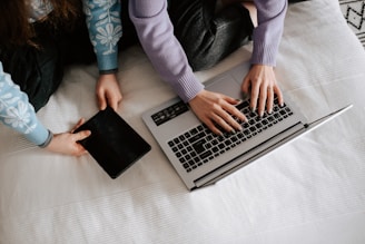 two people sitting on a bed using a laptop