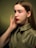 A young woman with long brown hair, wearing an olive green collared shirt, is posing with her hand gently touching her face. The background is a gradient of green shades, creating a soft, calming ambiance.