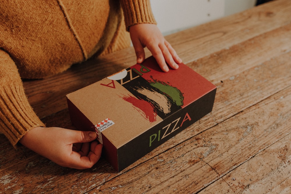 a person opening a pizza box on a wooden table