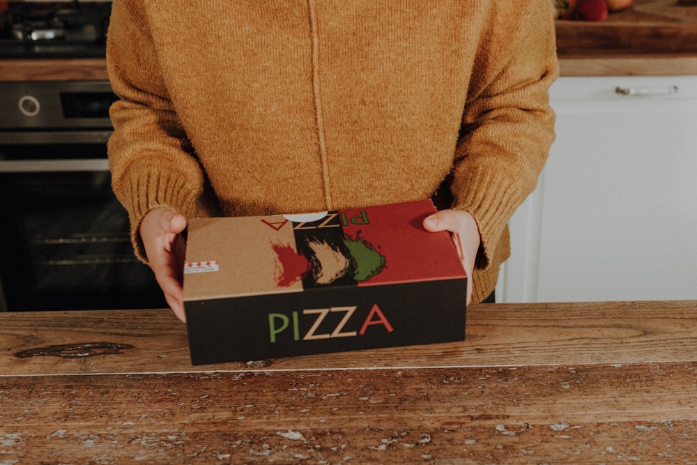 a person holding a pizza box in a kitchen