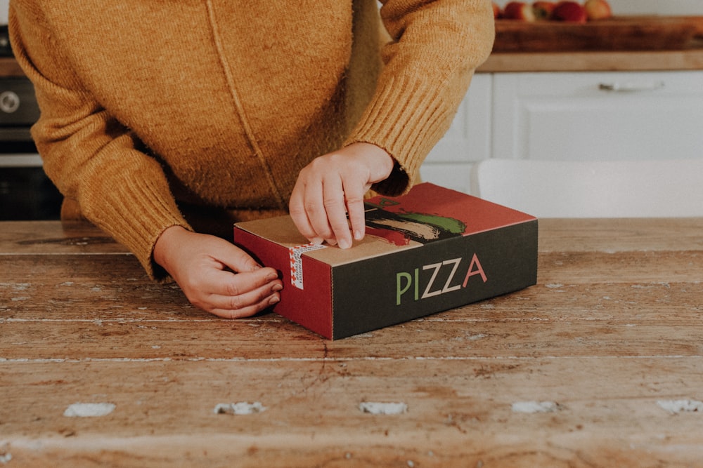 Eine Person, die eine Pizza in eine Schachtel auf einen Tisch stellt