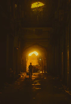 A shadowy nightclub alley in 1980s Johannesburg, featuring a silhouetted bouncer and a dancer illuminated by soft gold and burgundy light.