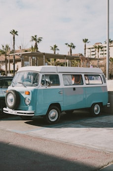 A pristine 1960s Volkswagen Transporter T1 parked on a sunlit vintage street, showcasing its classic rounded design and two-tone blue paint.