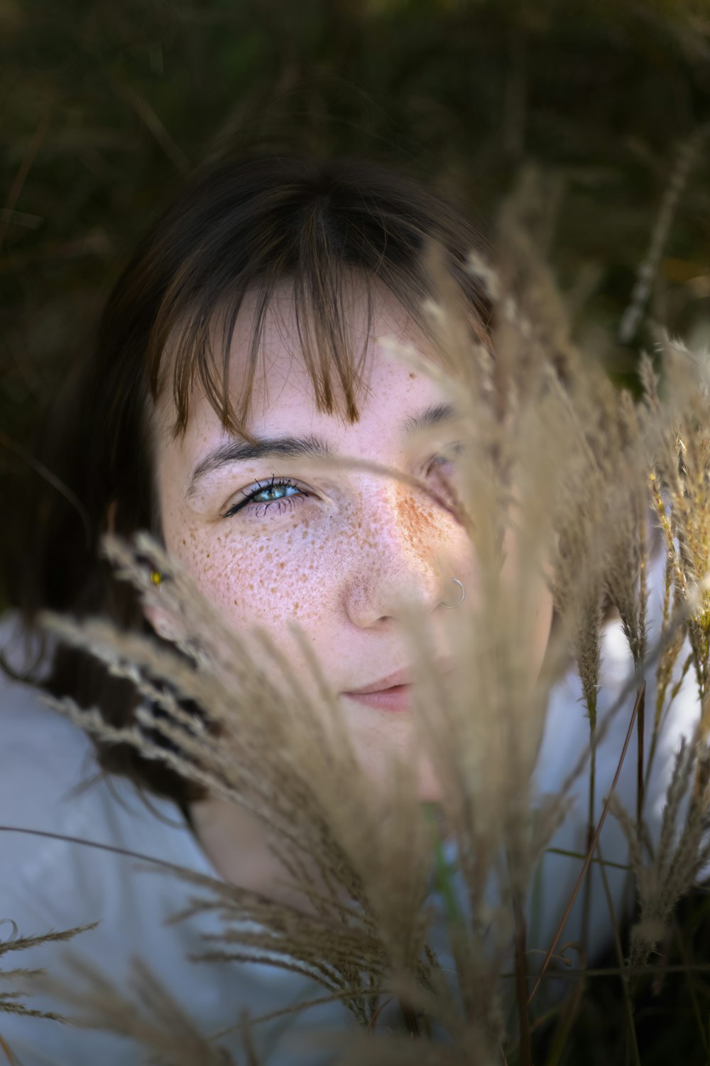 Eine Frau mit Sommersprossen im Gesicht versteckt sich hinter hohem Gras