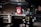 A commercial kitchen with stainless steel countertops and kitchen equipment, including a griddle and a dish rack holding a large red and white sign. Various kitchen tools and appliances are visible, such as knives in a holder, a bottle of cleaning liquid, and switches on the wall.