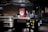 A commercial kitchen with stainless steel countertops and kitchen equipment, including a griddle and a dish rack holding a large red and white sign. Various kitchen tools and appliances are visible, such as knives in a holder, a bottle of cleaning liquid, and switches on the wall.