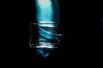 Close-up of a sleek glass bottle filled with clear hydrosol, set against a dark background with soft gradient lighting.