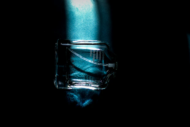 Close-up of amber glass spray bottle glowing softly against a dark charcoal backdrop with subtle art deco patterns.