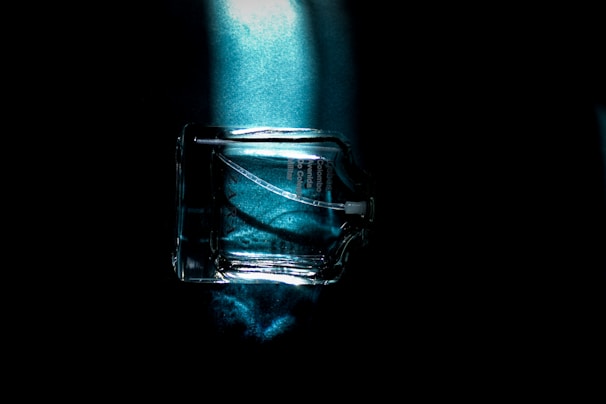 Close-up of a sleek glass bottle filled with clear hydrosol, set against a dark background with soft gradient lighting.