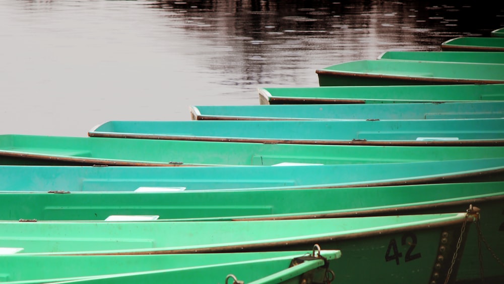 a row of green boats sitting on top of a lake