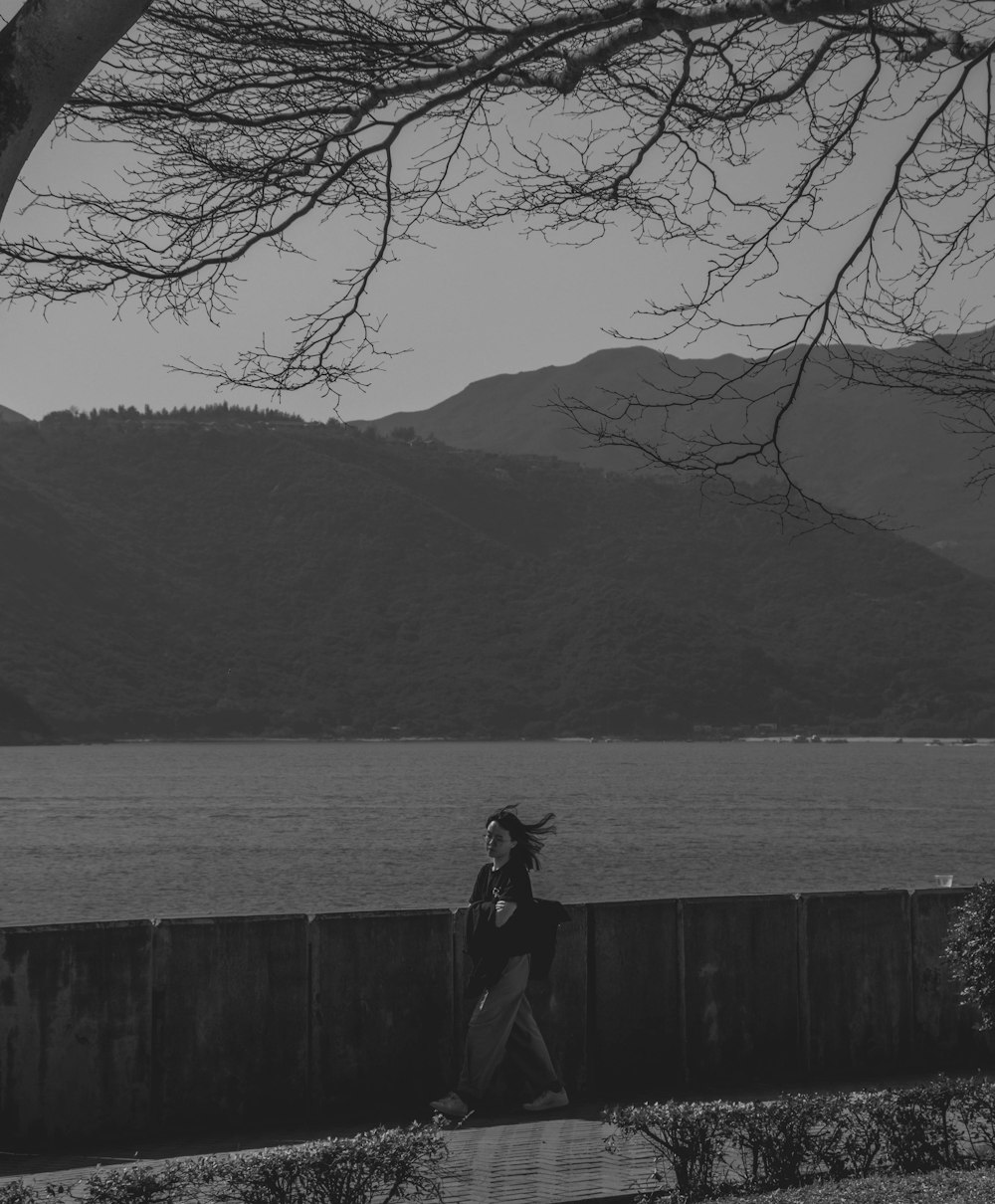 a black and white photo of a woman walking by the water