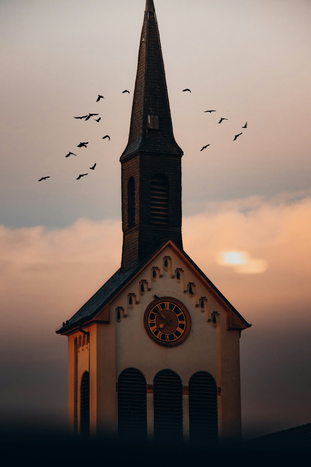 a church steeple with a clock and a flock of birds flying in the sky