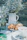 A peaceful outdoor setting featuring a table adorned with delicate blue flowers in glass jars and a ceramic pitcher. Fresh croissants rest on a white plate beside a cup of tea, creating a serene breakfast or brunch atmosphere.