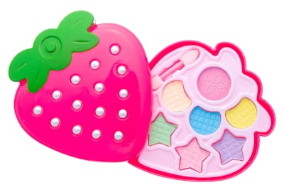 A pink, strawberry-shaped makeup kit with a green leafy top, featuring compartments with pastel-colored eyeshadows and shapes like stars and circles. The design is playful and colorful, aimed at children.